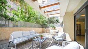 A covered outdoor patio with a sofa, chairs, and a table. - Garden Kalisher 3BR near the Beach by HolyGuest (Tel Aviv-Yafo)