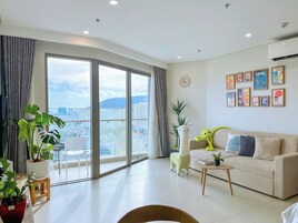 Amplia sala de estar con un gran ventanal corredero que da a un balcón, un sofá, una mesa de centro y varios objetos decorativos.