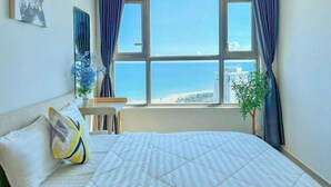 A bedroom with a large bed, a window with a view of the sea, and a plant on the windowsill. - Ngân Nguyễn Apartment - The Sóng Vũng Tàu (Ho Chi Minh City)