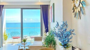 A dining area with a table set for two, a view of the sea through large windows, and a decorative wall piece. - Ngân Nguyễn Apartment - The Sóng Vũng Tàu (Ho Chi Minh City)