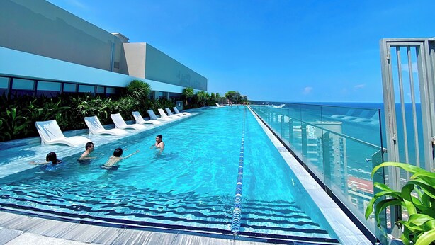 A pool with clear blue water, lounge chairs, and a glass railing overlooking the ocean. - Ngân Nguyễn Apartment - The Sóng Vũng Tàu (Ho Chi Minh City)
