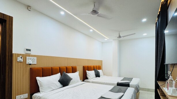 A hotel room with two beds, a wooden headboard, a small bedside table, a TV, and a ceiling fan. - Hotel Krishna Continental  (Prayagraj)