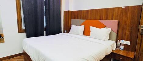 A neatly made bed with a wooden headboard, a bedside table with a bottle, and a window with curtains.
