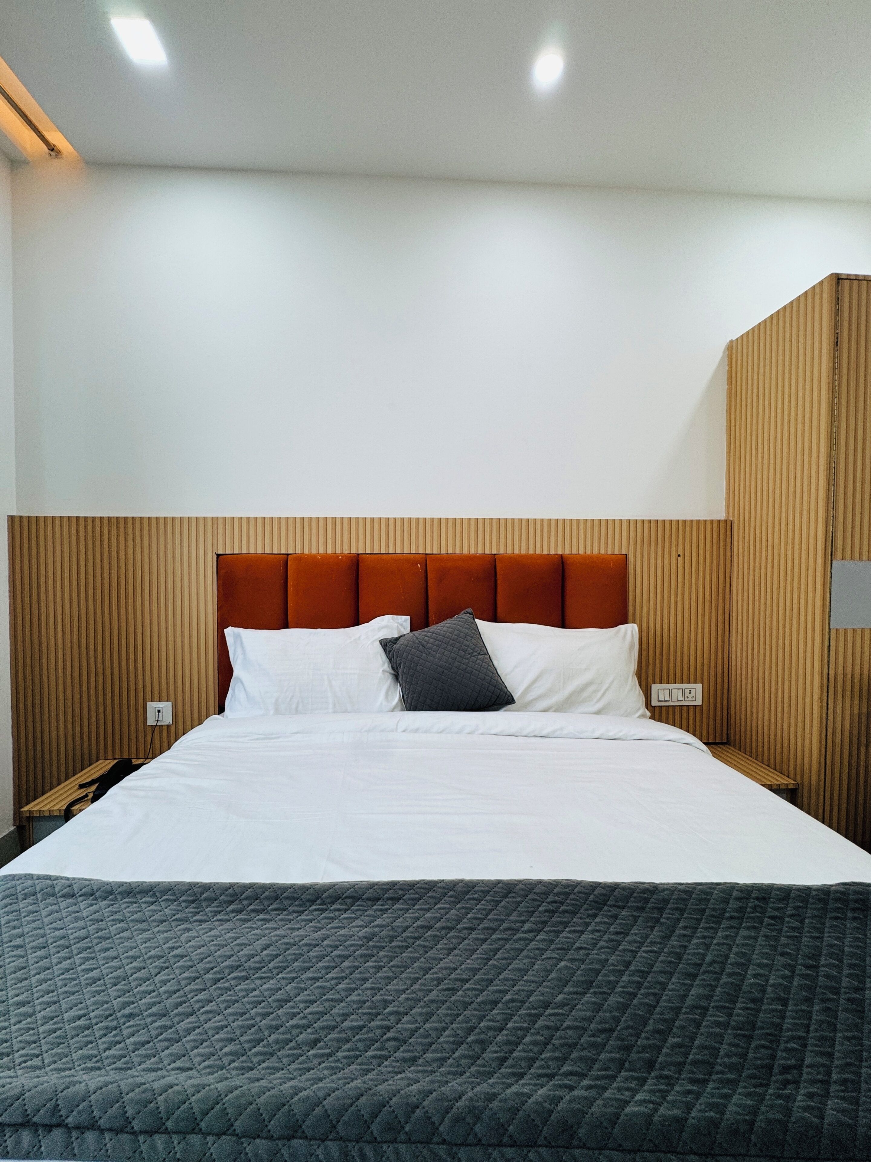 A hotel room with a bed, a wooden headboard, a nightstand, and a wall-mounted light fixture.