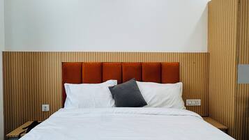 A hotel room with a bed, a wooden headboard, a nightstand, and a wall-mounted light fixture.