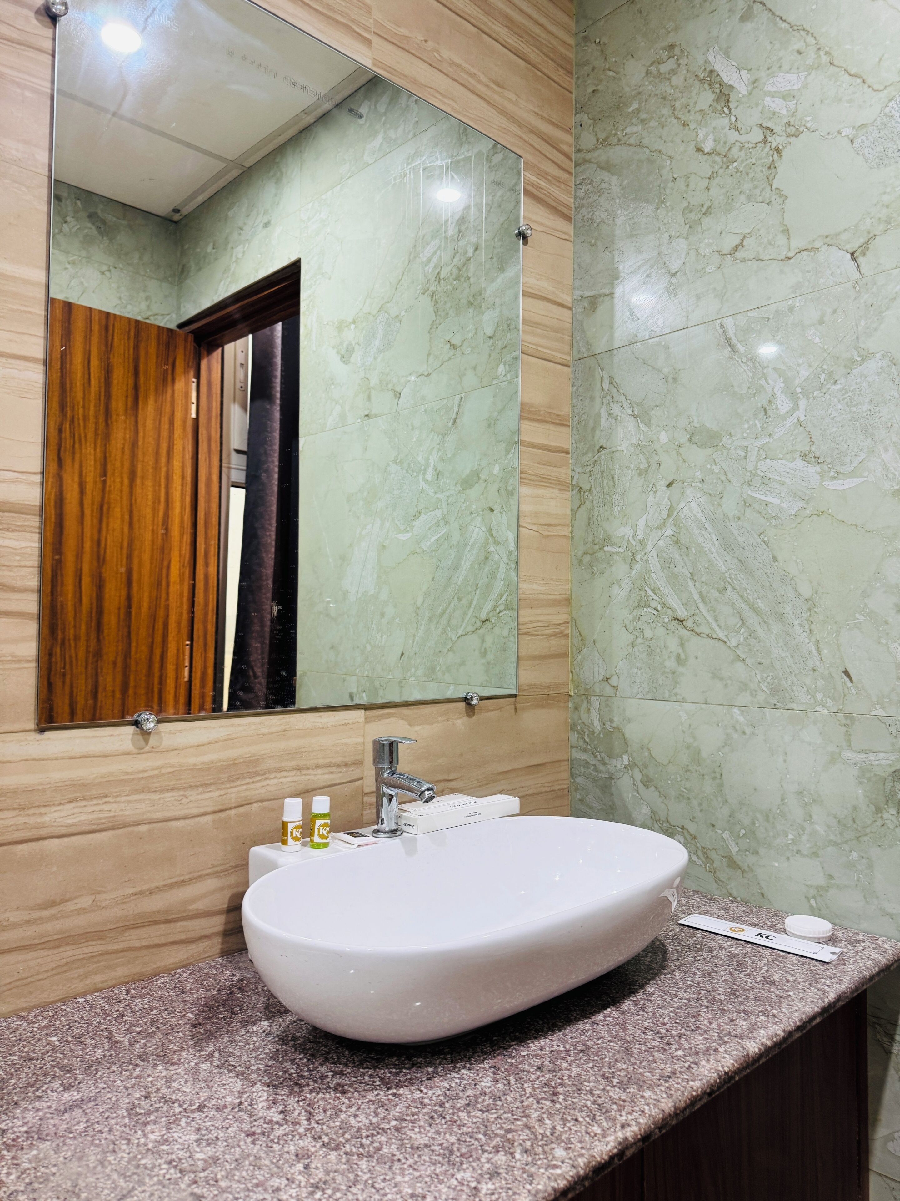 A bathroom with a marble wall, a sink with a mirror above it, and a wooden door.