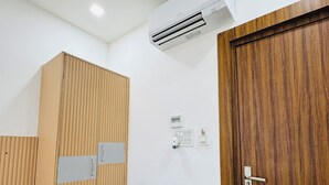 A compact room with a wooden wardrobe, a desk with a chair, an air conditioning unit, and a door. - Hotel Krishna Continental  (Prayagraj)