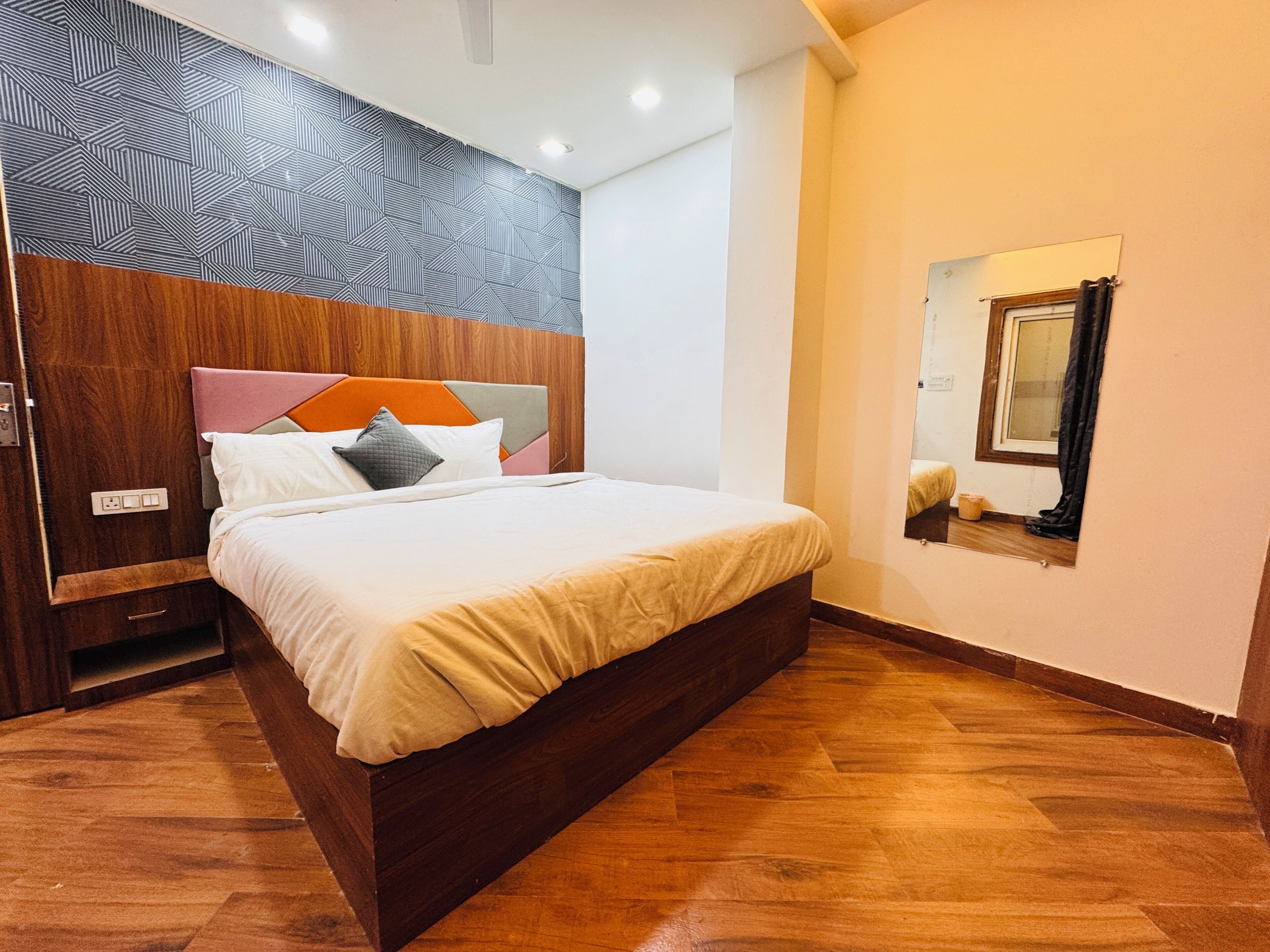 Un dormitorio moderno con cabecera de madera, una cama grande con muchos almohadones y mesita de noche integrada, además de un espejo en la pared.