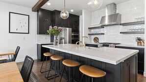 Een moderne keuken met donkere kasten, een groot kookeiland met barkrukken, roestvrijstalen apparatuur en hanglampen.