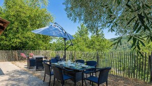 En udendørs terrasse med et bord, stole, en blå parasol og et træhegn.