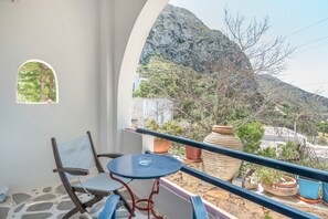 A balcony with a table and chairs, potted plants, and a view of a mountainous landscape. - Room 19 at Pagali Hotel in Amorgos (Órmos Aiyialís)