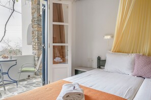 Habitación de hotel con cama, una mesita con sillas, pared de piedra y vistas al exterior.