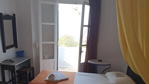 Ein Hotelzimmer mit zwei Betten, einem Schreibtisch, einem Stuhl, einem kleinen Tisch und einer Tür, die nach draußen führt.