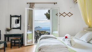 A hotel room with a bed, a desk, a chair, a small table, and a view of the sea through an open door. - Room 15 at Pagali Hotel with King Bed (Órmos Aiyialís)