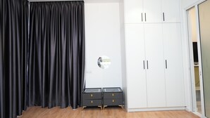 Ein Zimmer mit schwarzem Vorhang, einem weißen Kleiderschrank und zwei Nachttischen mit Schubladen.