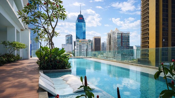Ein Pool auf dem Dach mit Blick auf eine Stadtlandschaft, umgeben von Grünflächen und modernen Gebäuden.