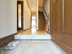 Um corredor com piso de mármore, porta de madeira e um par de chinelos.