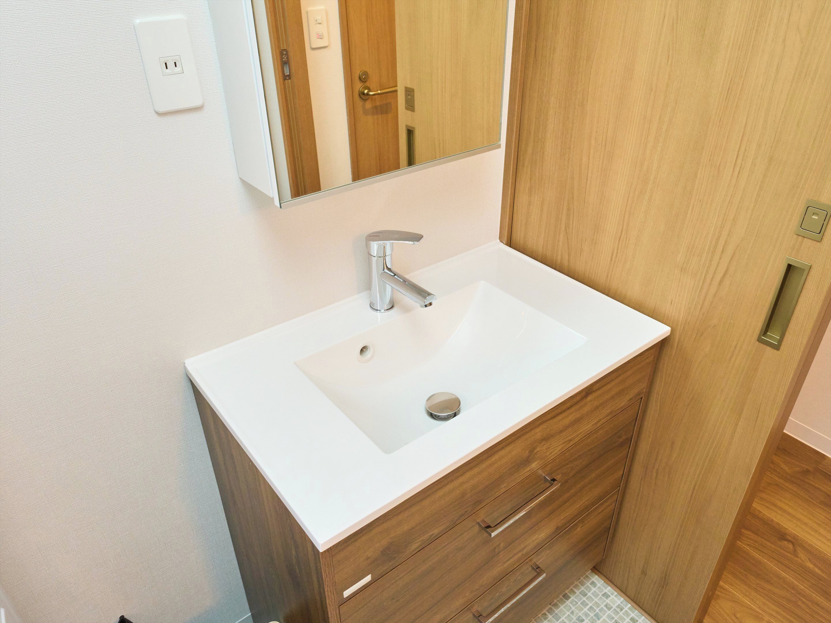 Un baño con un lavamanos blanco, un espejo, un armario de madera y una puerta.