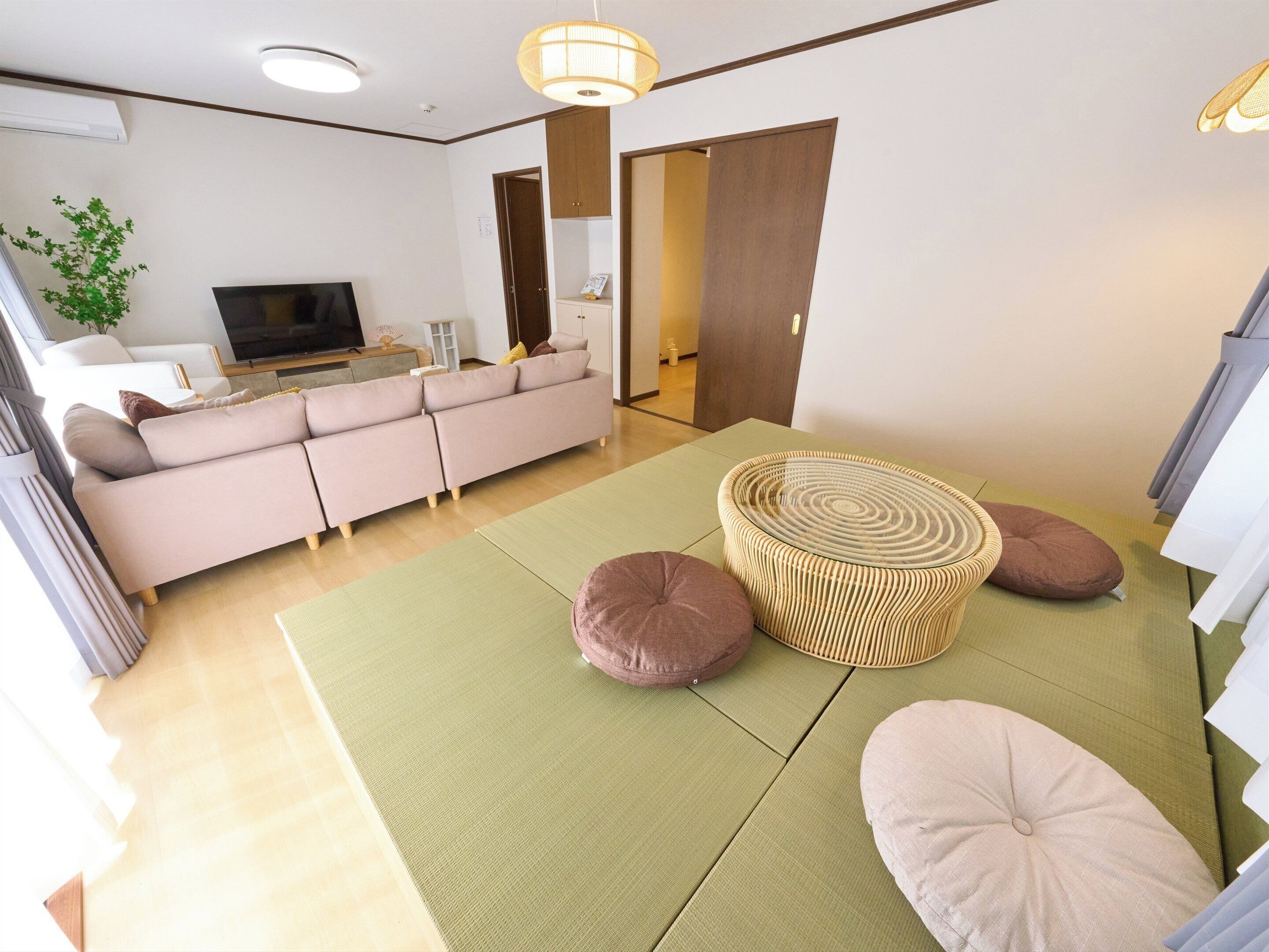 A living room with a sofa, a television, a wall-mounted shelf, and a woven coffee table.