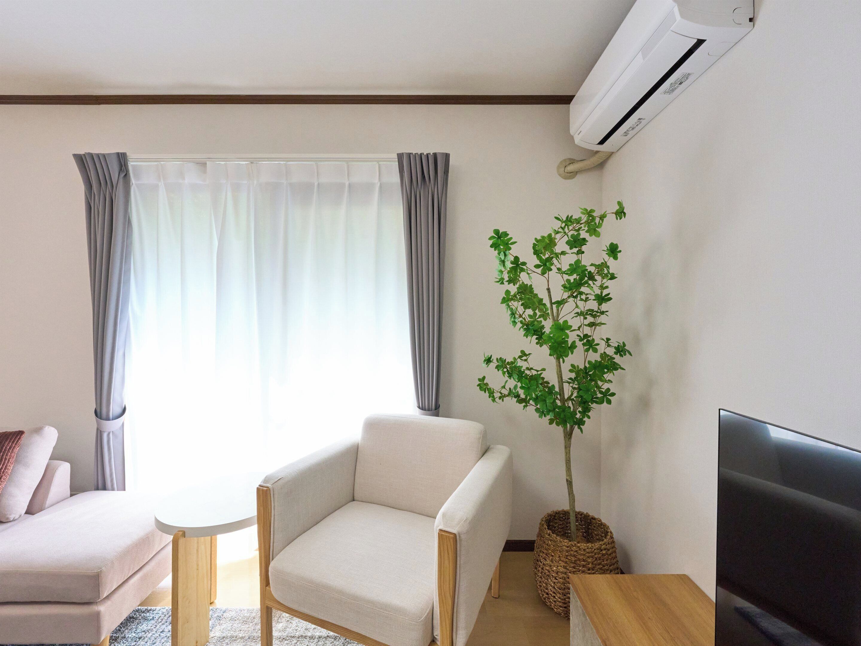 A living room with a sofa, armchair, small table, potted plant, and a TV.