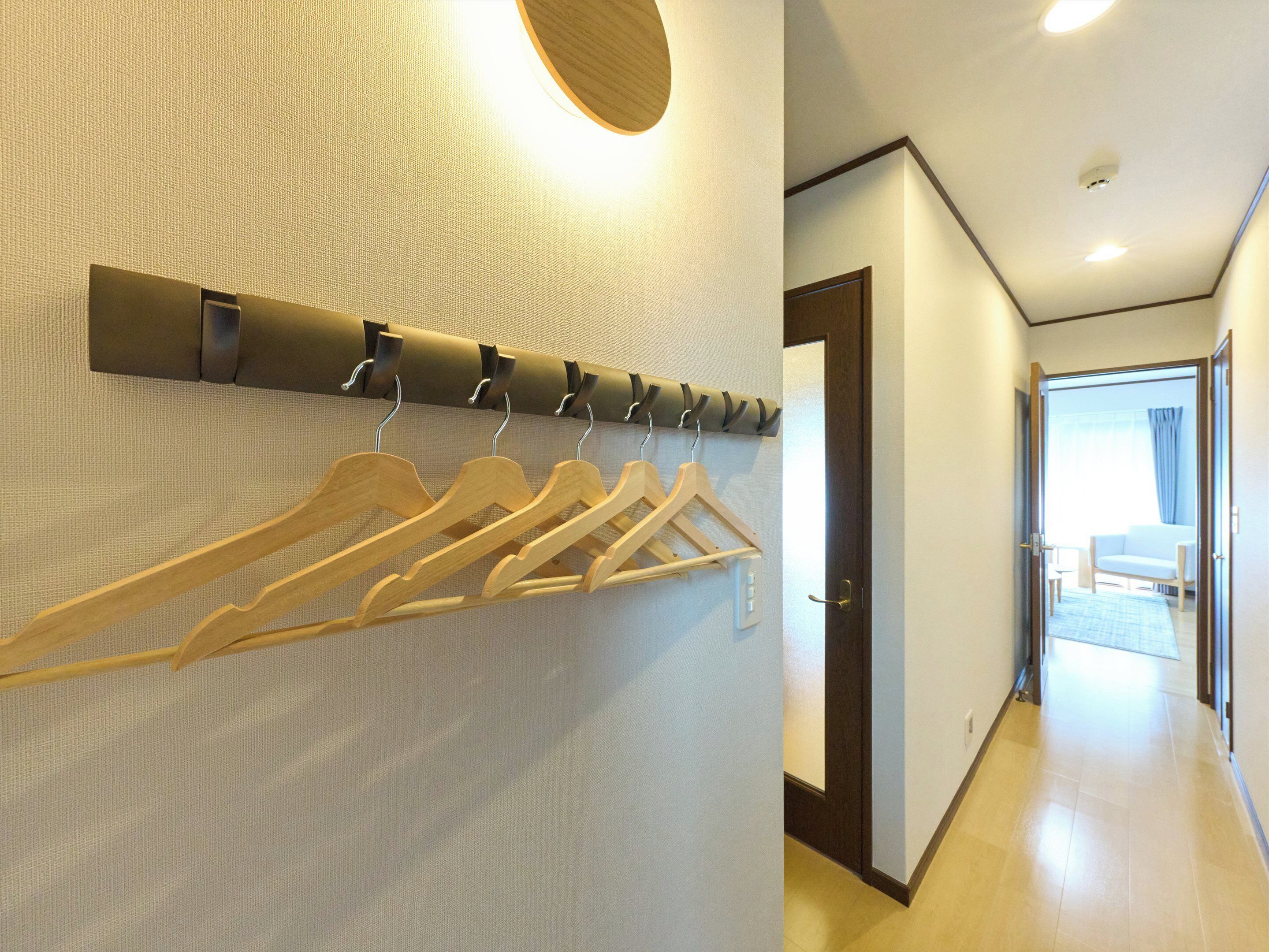 A hallway with a coat rack, a door, and a view into a room with a bed and a window.