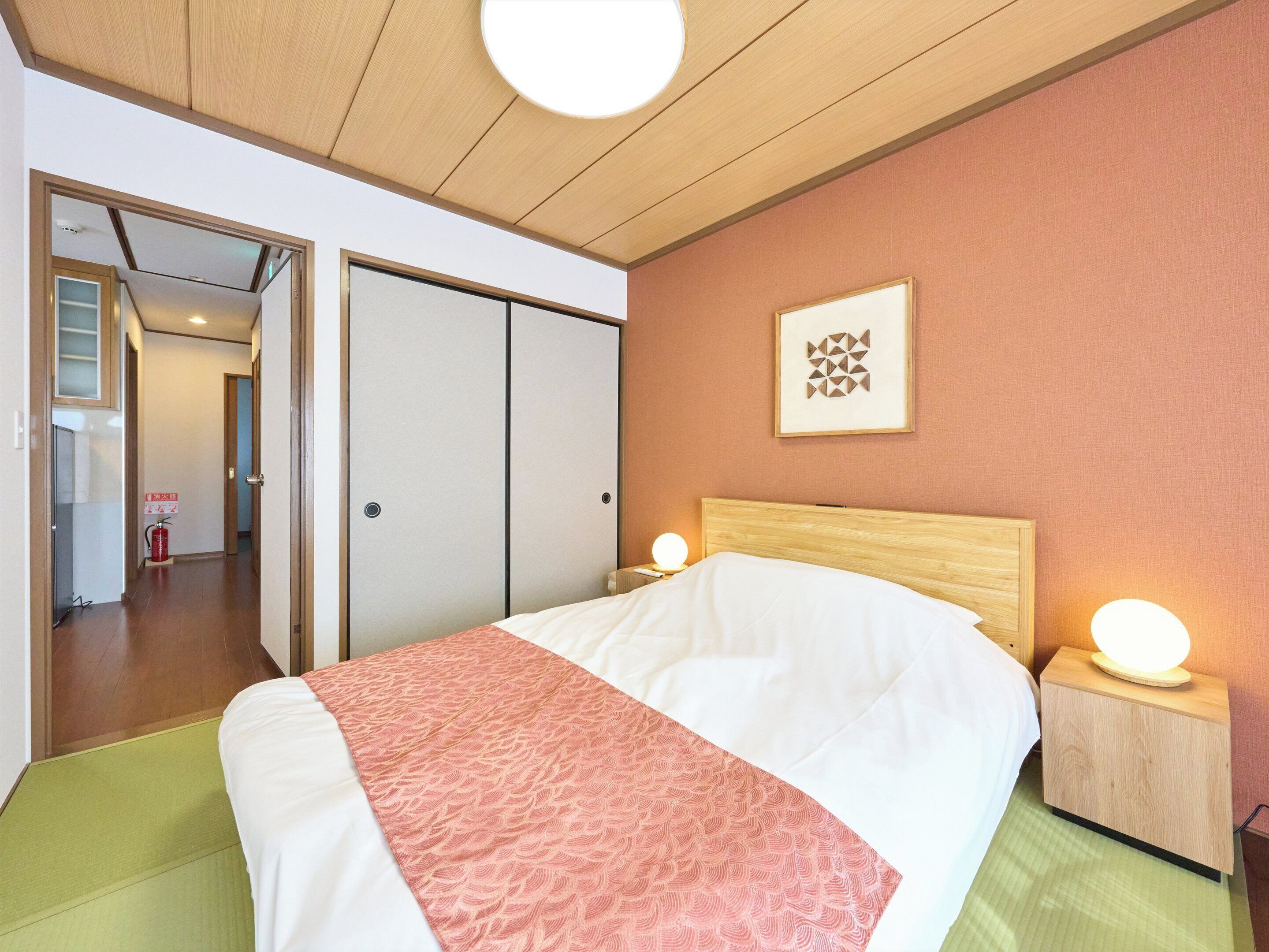 A hotel room with a bed, bedside lamps, a framed picture on the wall, and a door leading to another room.