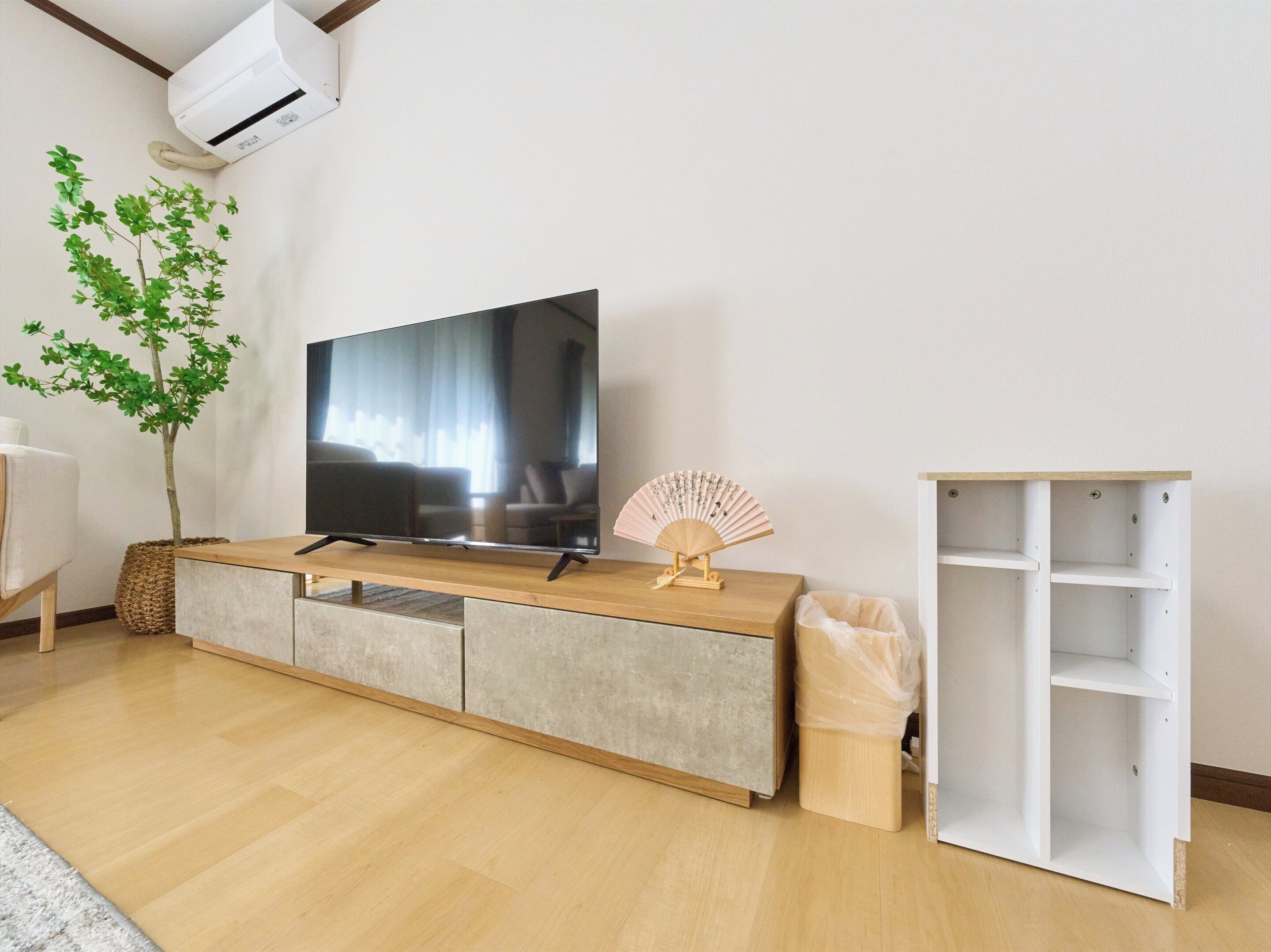 Un salon avec un téléviseur à écran plat posé sur une console en bois, un petit ventilateur et une plante.