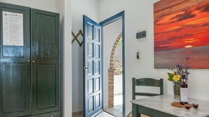 Una stanza con una porta verde, una porta blu, un tavolo con una bottiglia e dei bicchieri, e un quadro raffigurante un tramonto.