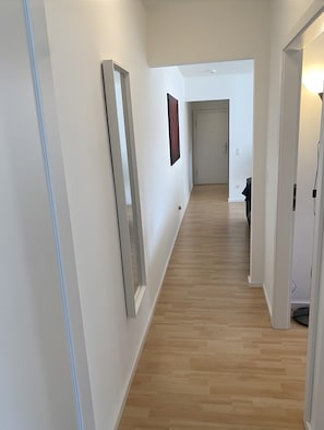 A hallway with a wooden floor, white walls, and a door at the end. - Cozy Apartment in Hannover – Near City, Fair, MHH with Balcony and Wi-Fi (Hannover)