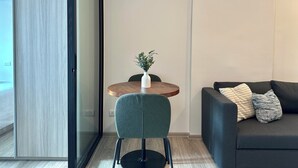 A modern living room with a round wooden table, a green chair, and a dark sofa with patterned cushions. - Modern, Fully Equipped 1BR in Bangna/Sukhumvit (Krung Thep Maha Nakhon)