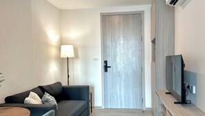 A modern living room with a sofa, a lamp, a TV, and a wooden cabinet. - Modern, Fully Equipped 1BR in Bangna/Sukhumvit (Krung Thep Maha Nakhon)