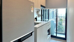 A modern kitchen with a stainless steel refrigerator, wooden cabinets, and a large window offering a view of the city. - Modern, Fully Equipped 1BR in Bangna/Sukhumvit (Krung Thep Maha Nakhon)