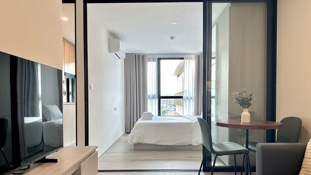 A modern hotel room with a bed, a TV, a desk, a chair, and a small table with a vase. - Modern, Fully Equipped 1BR in Bangna/Sukhumvit (Krung Thep Maha Nakhon)