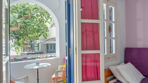 Een kamer met een paarse bank, een kleine ronde tafel, een raam met roze gordijnen en uitzicht op een boom.