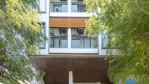 Um edifício moderno de vários andares com varandas, janelas amplas e uma área de entrada coberta.