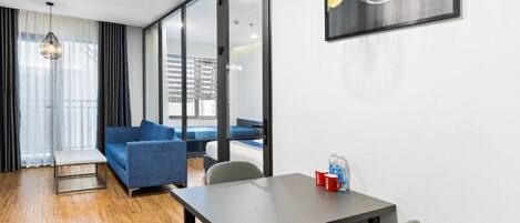 Una habitación moderna con sofá, mesa de comedor con sillas, mesa de centro y un amplio ventanal con cortinas.