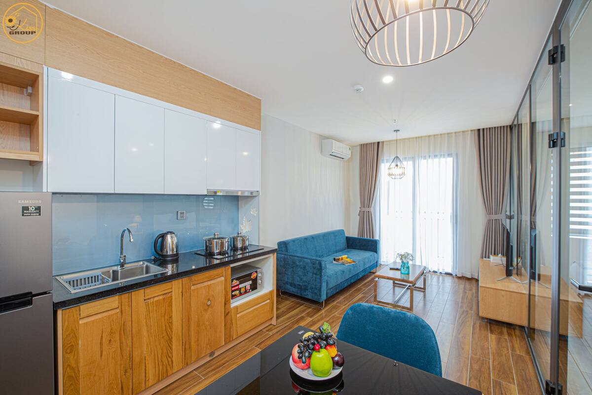 A modern kitchen with white cabinets, a Samsung refrigerator, and a dining area with a blue sofa and a table with fruit.