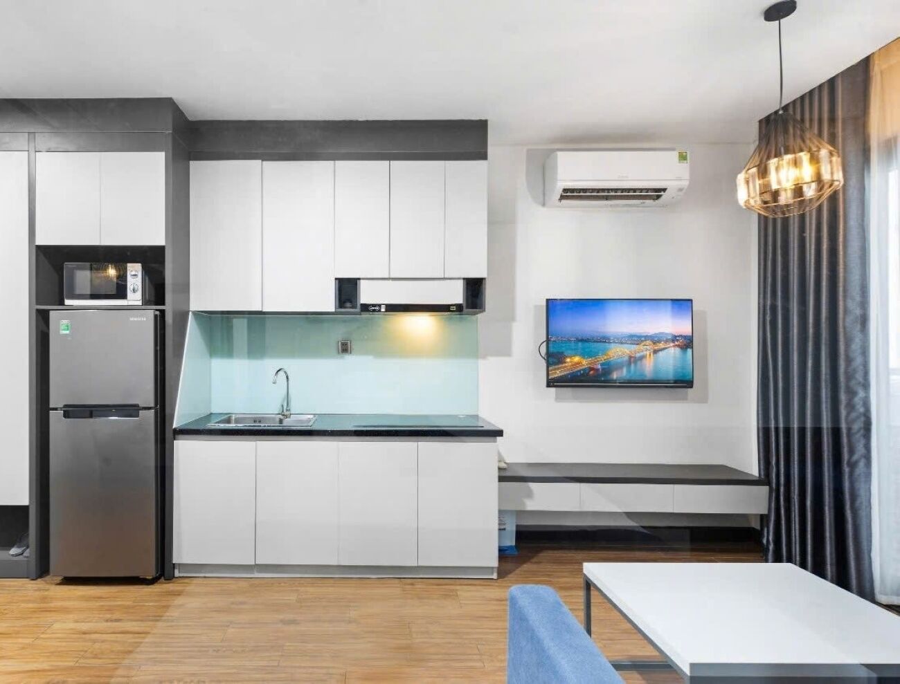 A modern kitchen with a built-in microwave, a stainless steel refrigerator, and a flat-screen TV mounted on the wall.