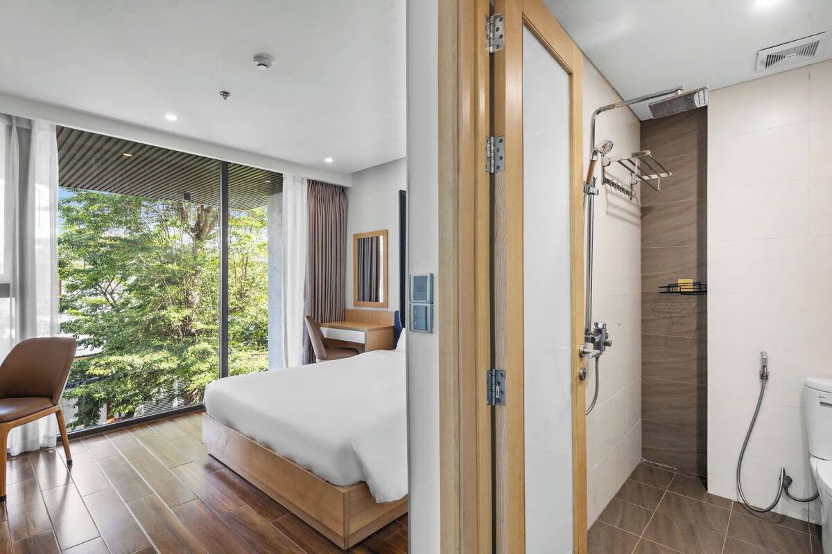 A modern bedroom with a large bed, a desk, and a view of trees.