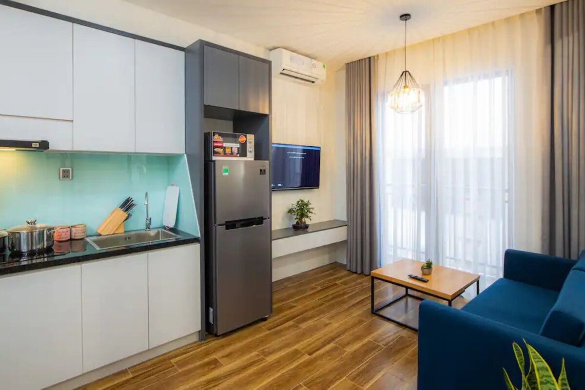 A modern kitchen with a built-in refrigerator, a dining area with a blue sofa, and a TV mounted on the wall.