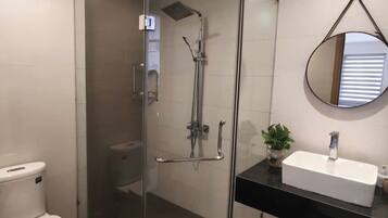 A modern bathroom with a glass-enclosed shower, a white toilet, a black countertop, and a round mirror.