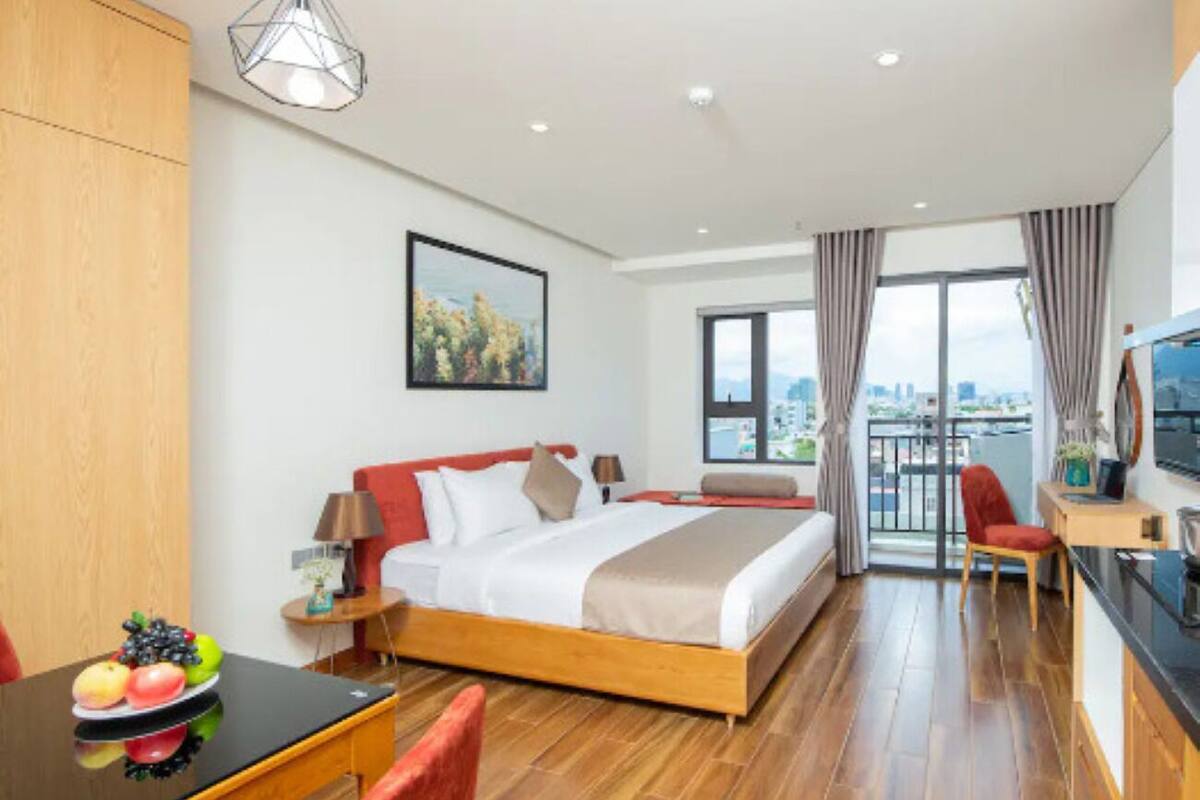 A hotel room with a bed, a desk, a chair, a dining table with fruit, a TV, and a city view.