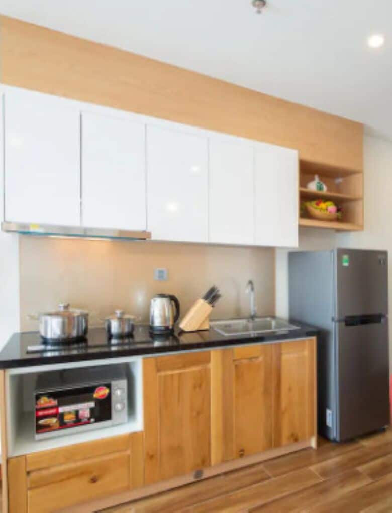 Una cocina moderna con gabinetes blancos, encimera negra, microondas integrado y refrigerador de acero inoxidable.