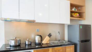 Una cocina moderna con gabinetes blancos, encimera negra, microondas integrado y refrigerador de acero inoxidable.