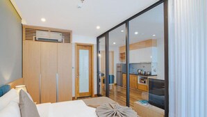 Quarto de hotel com cama, guarda-roupa, cozinha compacta e porta de correr para o exterior.