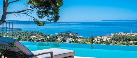 An infinity pool with a view of a coastal town and the sea.