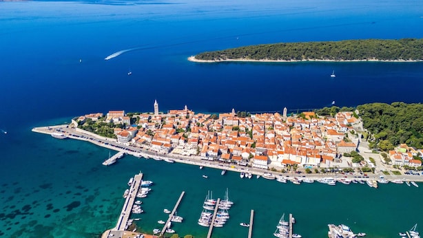 An aerial view of a coastal town with a marina, buildings with red-tiled roofs, and a prominent tower. - Vila Pantovcak with stunning views by Villas Guide (Mundanije)