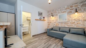A modern living room with a stone wall, a grey sofa, a wooden floor, and a door leading to a bathroom.