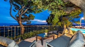 A poolside area with outdoor furniture, a view of the sea, and a large tree. - Vila Pantovcak with stunning views by Villas Guide (Mundanije)