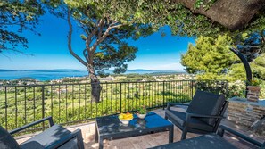 A balcony with outdoor furniture, a view of the sea, and a distant town.